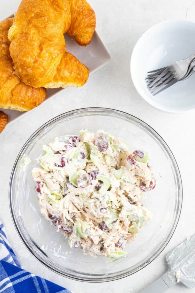 Overhead view of chicken salad ingredients combined in a clear mixing bowl.