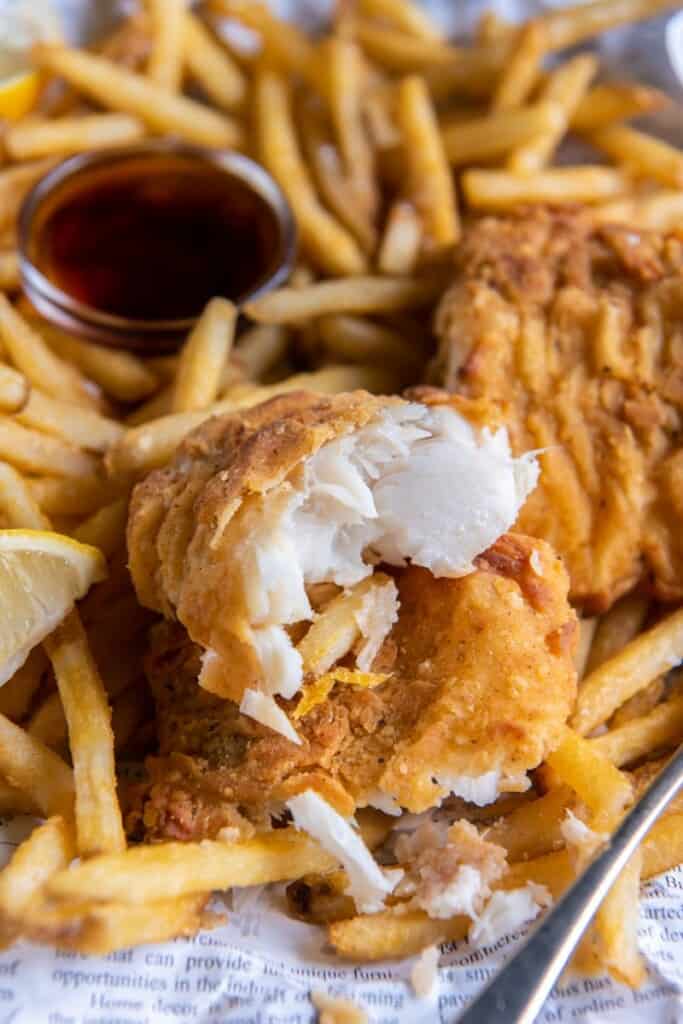 A basket of fish and chips, one cod filet cut in half, with lemon wedges and dipping sauce.