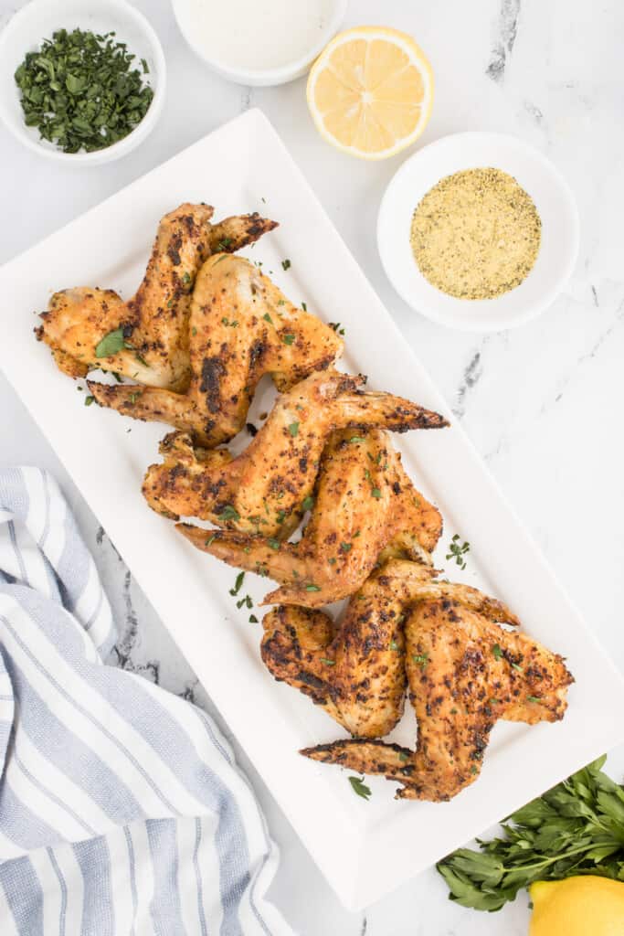 Seasoned chicken wings on a serving platter with dipping sauce next to it.