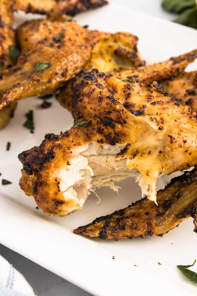 Close up view of a seasoned chicken wing with a piece pulled away to show the inside.