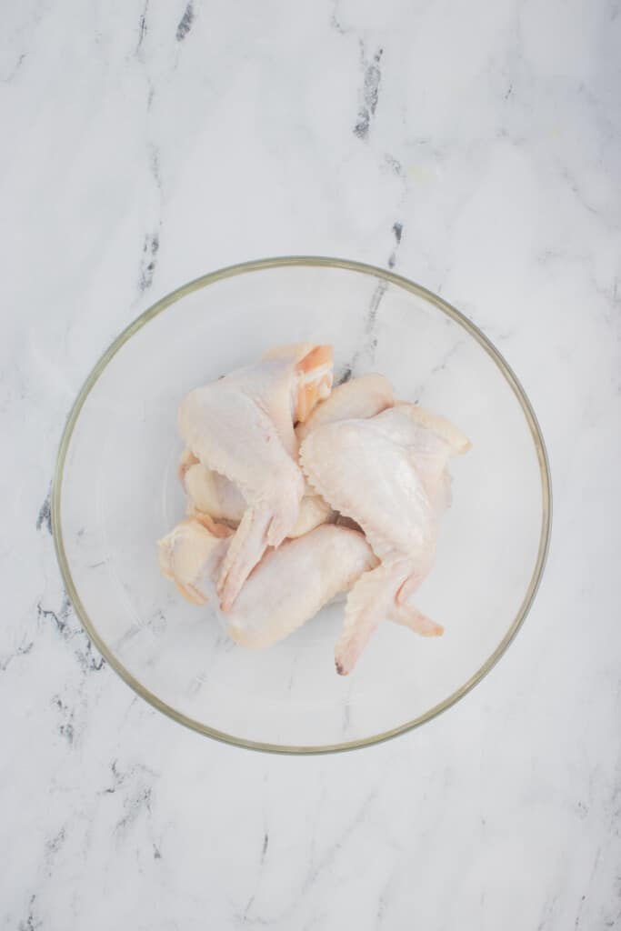 Chicken wings in a clear bowl after being patted dry to remove excess moisture.