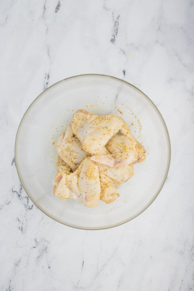 Seasonings added to chicken wings in a clear bowl.