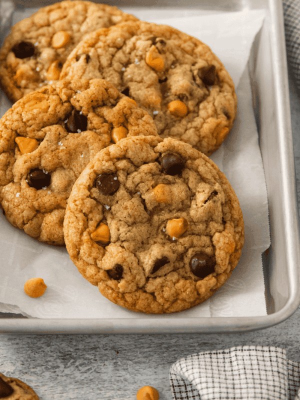 Four butterscotch chocolate chip cookies on a parchment lined baking sheet.