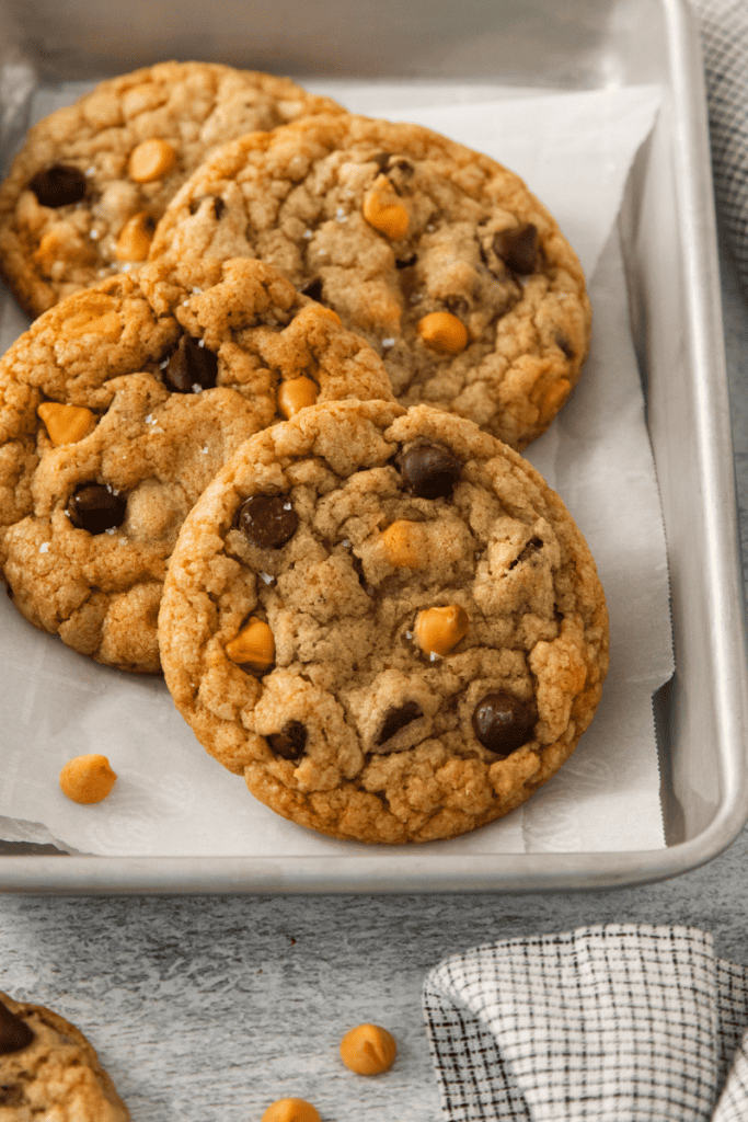 Four butterscotch chocolate chip cookies on a parchment lined baking sheet.