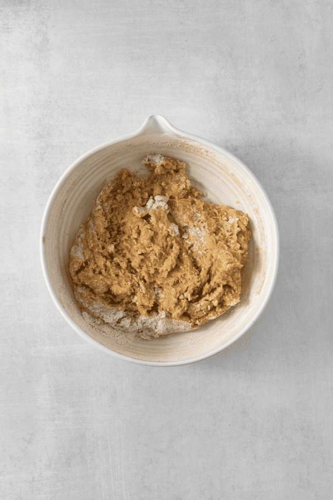 Adding chips to cookie dough in white mixing bowl.