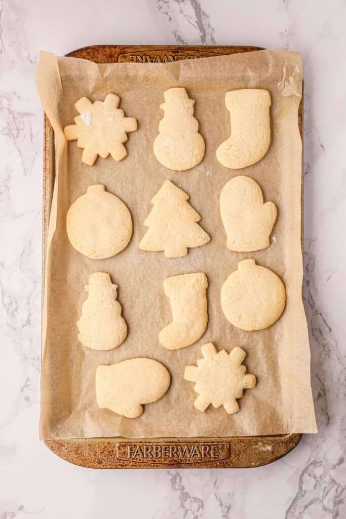 Twelve baked Christmas Shaped sugar cookies on a parchment lined baking sheet.