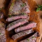 A New York Strip Steak cut into slices on a wooden cutting board.