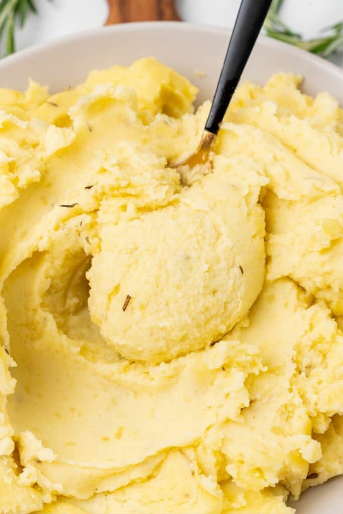 A bowl of seasoned mashed potatoes with a spoon lifting one bite.
