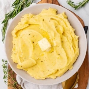 A serving bowl of rosemary seasoned mashed potatoes topped with butter.
