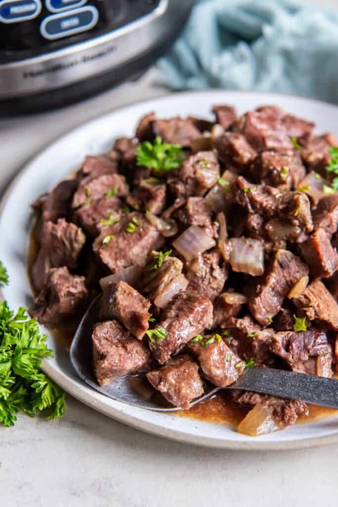 A ladle holding a scoop of steak bites that were prepared in a crock pot.