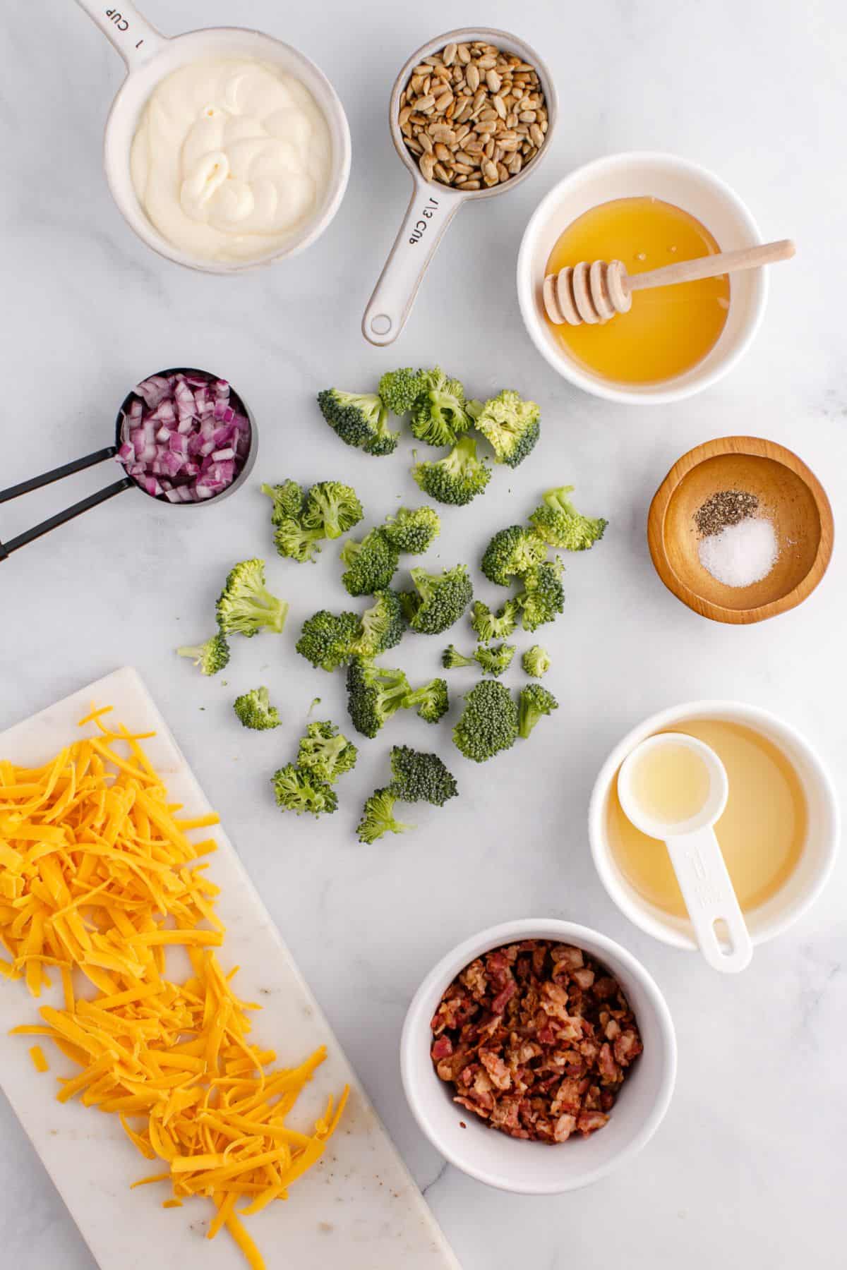 Ingredients needed to make broccoli salad: mayo, apple cider vinegar, honey, salt, pepper, broccoli, bacon, cheese, sunflower seeds, and onion.