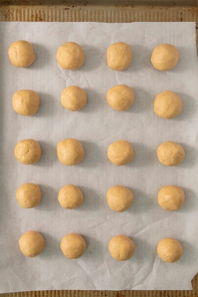 scooping out peanut butter balls onto baking sheet with parchment paper.