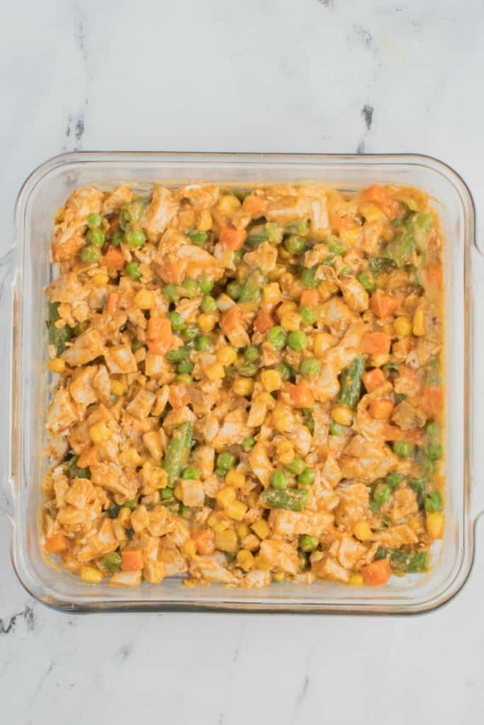 Combining the filling ingredients for chicken pot pie and spreading them evenly in a square baking dish.