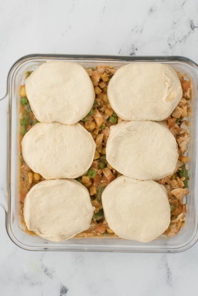 Placing biscuits on top of the chicken pot pie filling in a square baking dish.