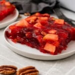 A serving of Cranberry Jello Salad on a serving dish with pecans in the foreground.