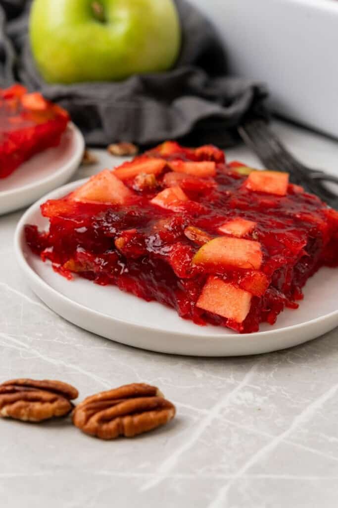 A serving of Cranberry Jello Salad on a serving dish with pecans in the foreground.
