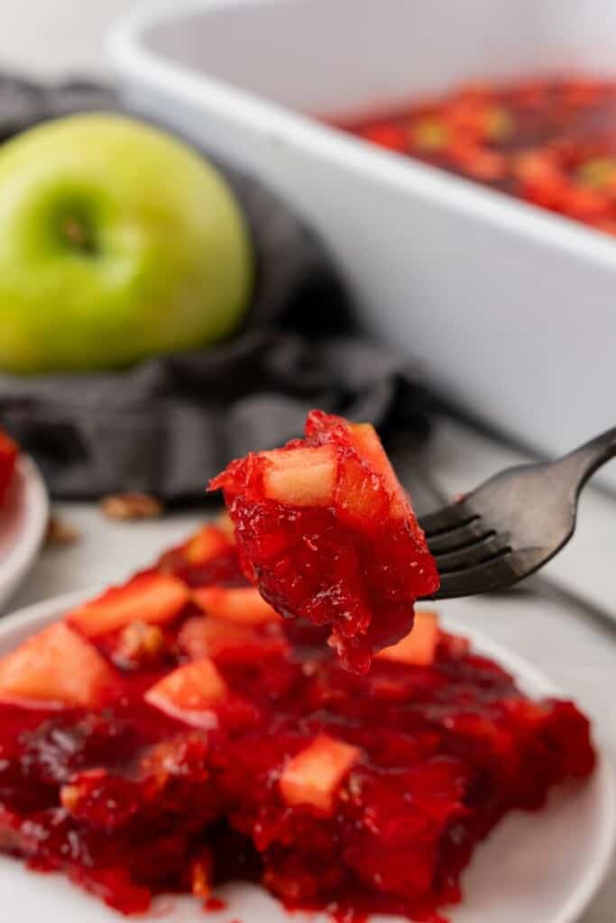 A fork lifting a single bite of cranberry jello salad off the plate holding a single serving.