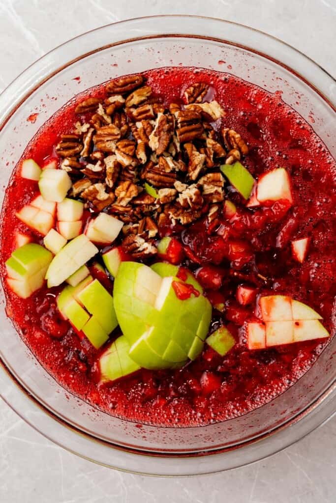 Apples and pecans added to jello mixture in a mixing bowl to be folded in.