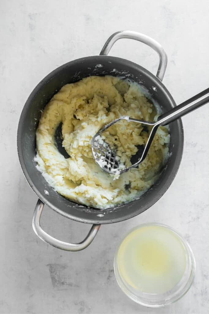 Slowly adding the potato water back into the mashed potatoes.