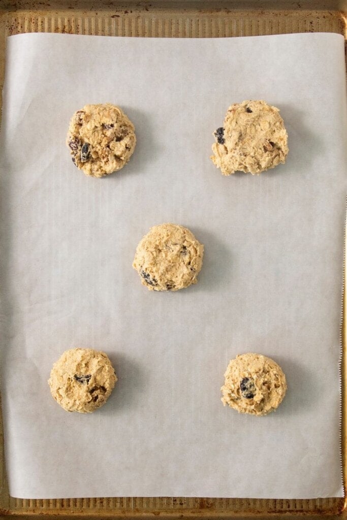 adding dollops of oatmeal cookie batter to parchment paper on sheet pan.