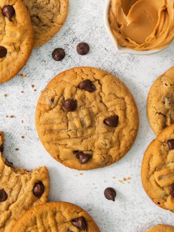 Chocolate Chip Peanut Butter Cookies resting on a flat surface with chocolate chips sprinkled around.