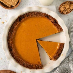 Sweet potato pie in a graham cracker crust with one slice taken out and another slice in the pie pan.