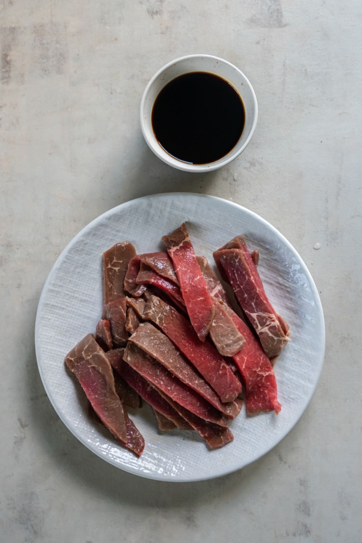 Sirloin steak cut into pieces on a white plate next to a small bowl of teriyaki sauce.
