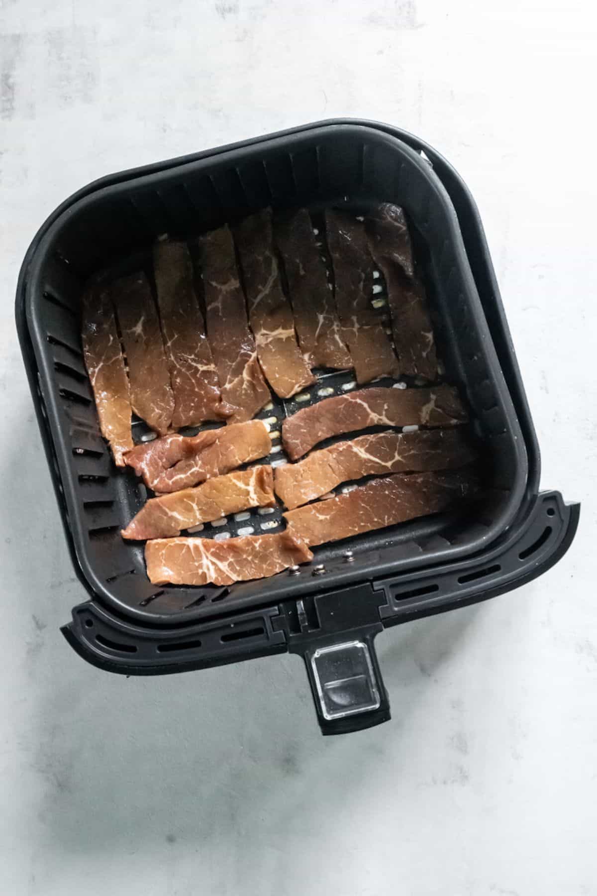 Sirloin steak pieces in a single layer of a black air fryer basket.