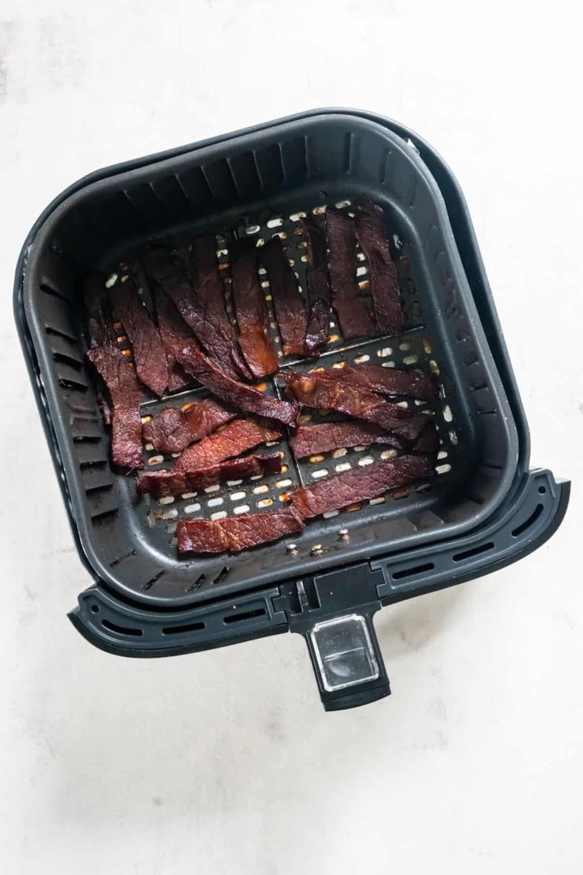 Cooked beef jerky in the air fryer basket.