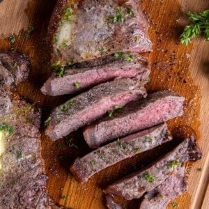 Overhead view of air fryer new york strip steak cut into strips with a dab of butter on top of an uncut steak.
