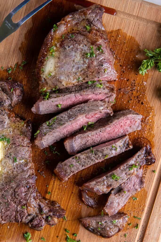 Overhead view of air fryer new york strip steak cut into strips with a dab of butter on top of an uncut steak.