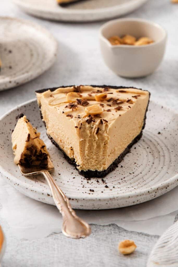 A piece of peanut butter pie on a plate with a forkful taken out of it and on the side.