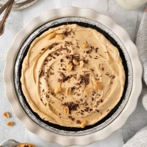 Peanut butter pie with cool whip in an Oreo crust topped with peanuts and chocolate shavings.