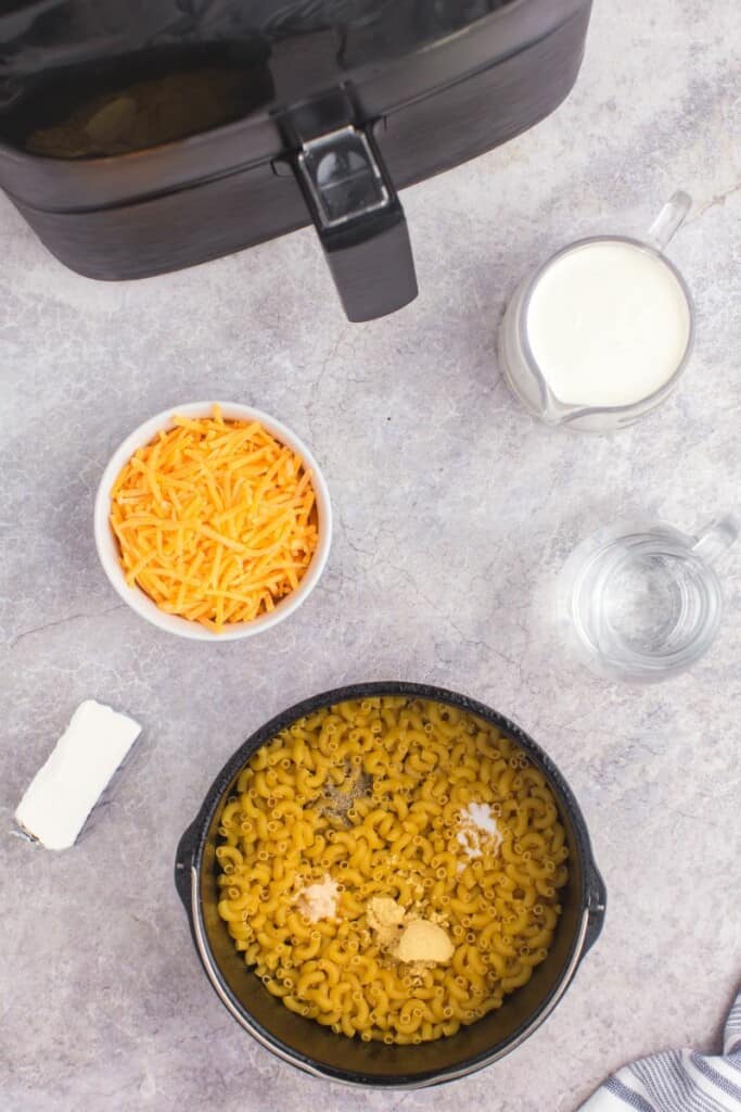 adding dry noodles and seasoning to air fryer pot.