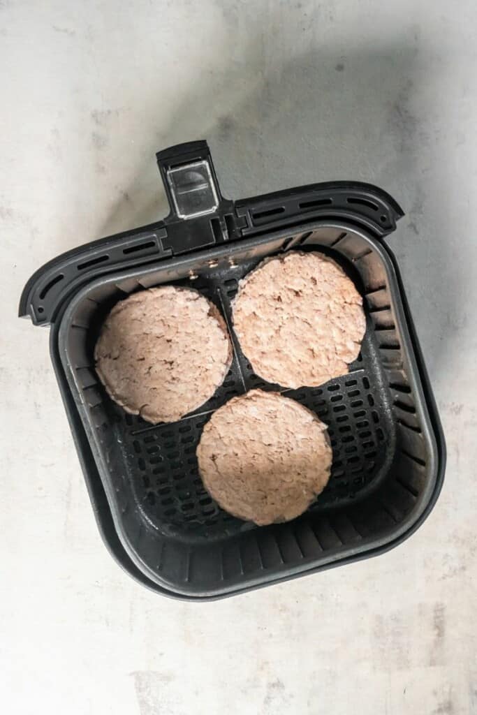 adding frozen turkey burgers in the air fryer basket.