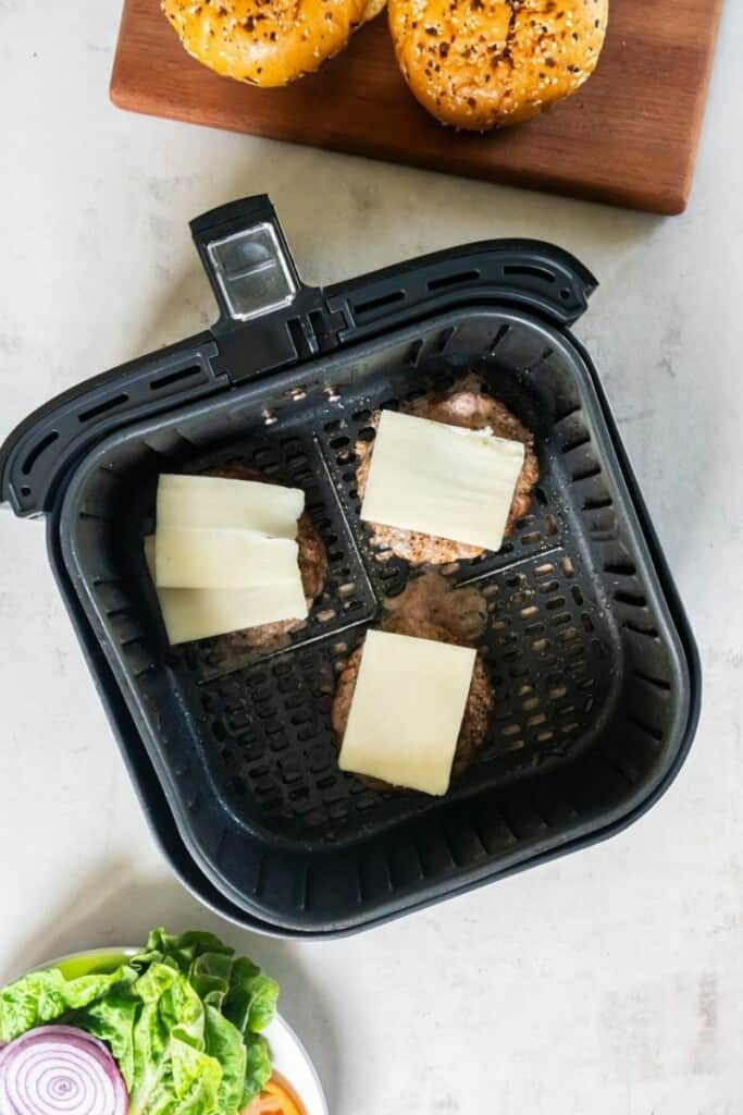 adding cheese slices to cooked turkey burgers.