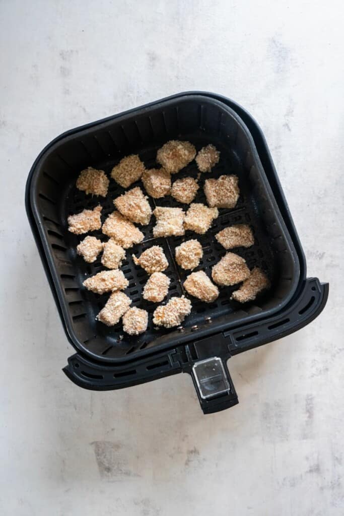 adding breaded fish bite to air fryer basket.