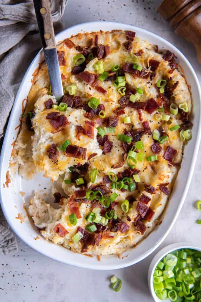 Overhead view of twice baked mashed potatoes in a white casserole dish with a scoop of it on a serving spoon.