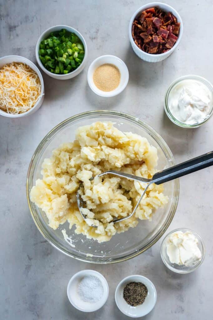 Potatoes being mashed in a clear bowl.