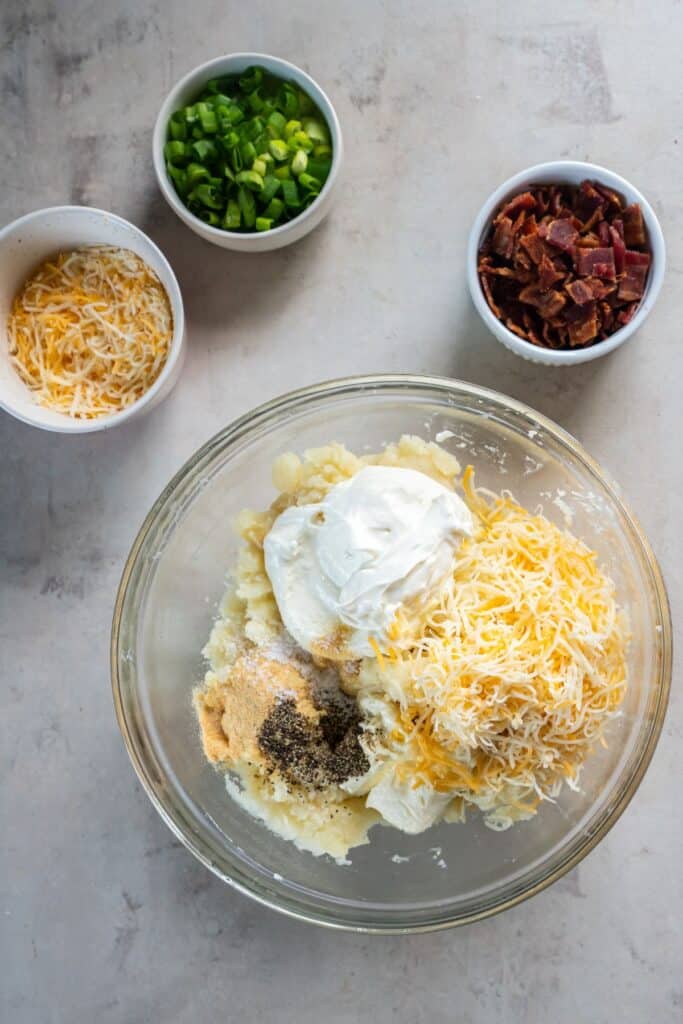 Mixing in the cheeses and seasonings to the mashed potatoes in a clear bowl.