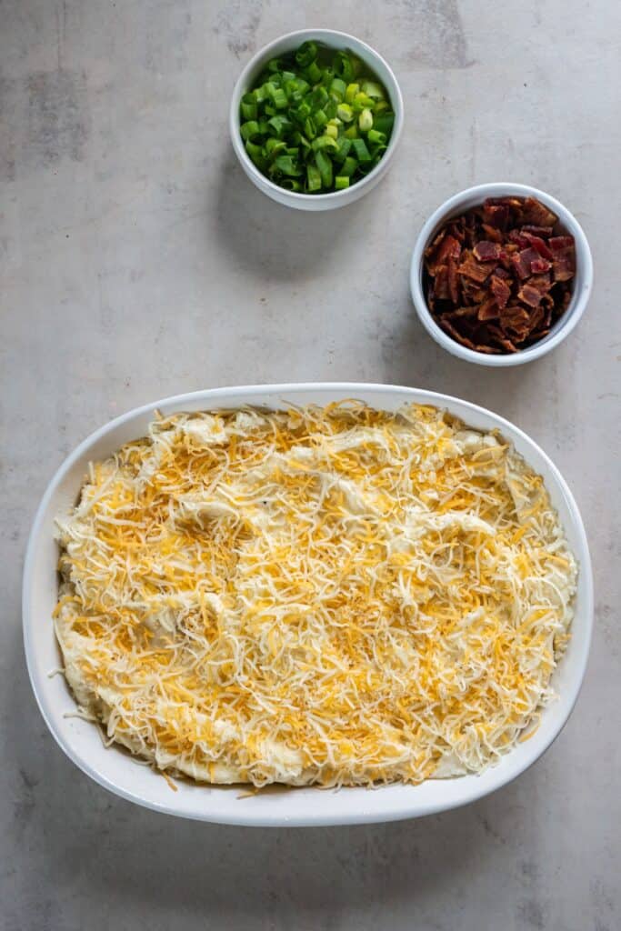The twice baked mashed potatoes in a casserole dish ready to be topped with bacon and baked.