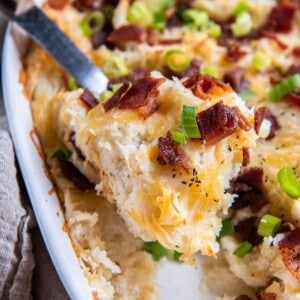 Twice baked mashed potatoes in a casserole dish being scooped out with a serving spoon.