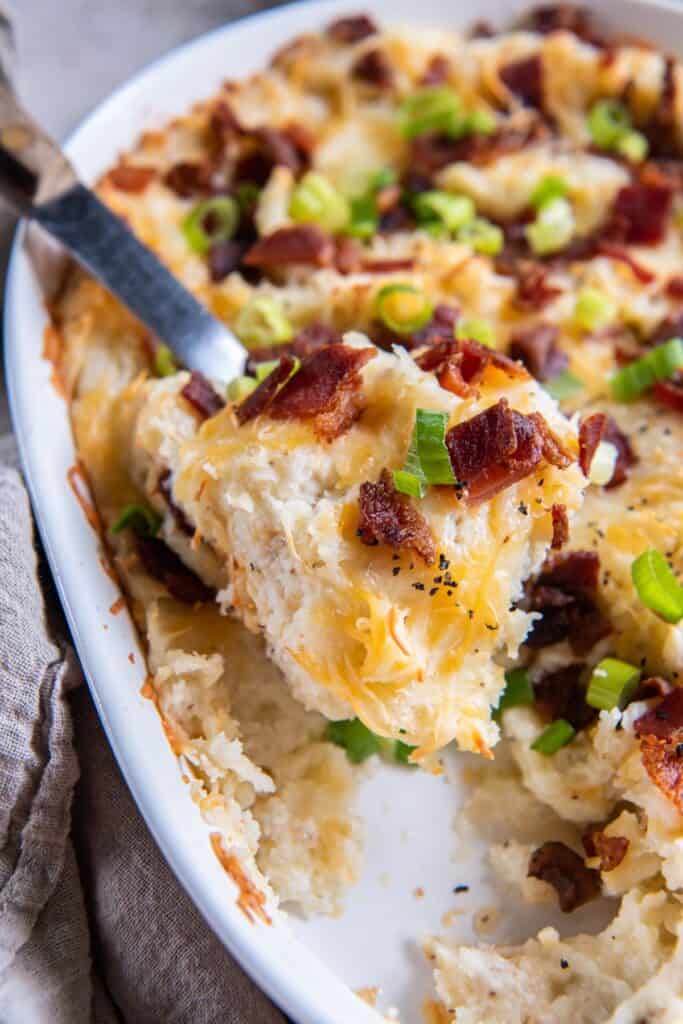 Twice baked mashed potatoes in a casserole dish being scooped out with a serving spoon.