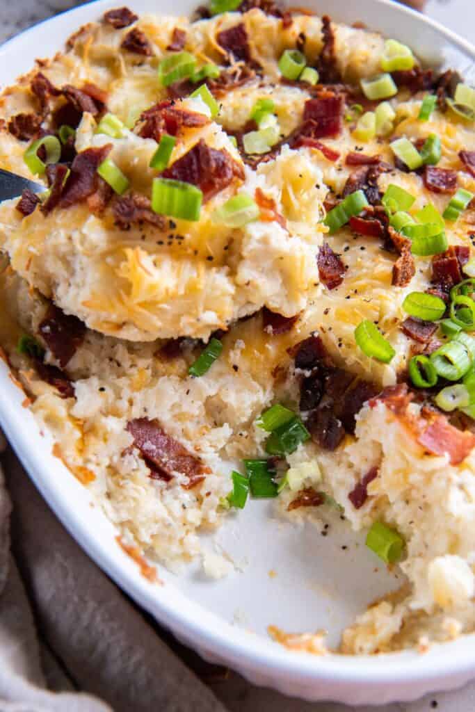 Scoop of double baked mashed potatoes being scooped out of a casserole dish.