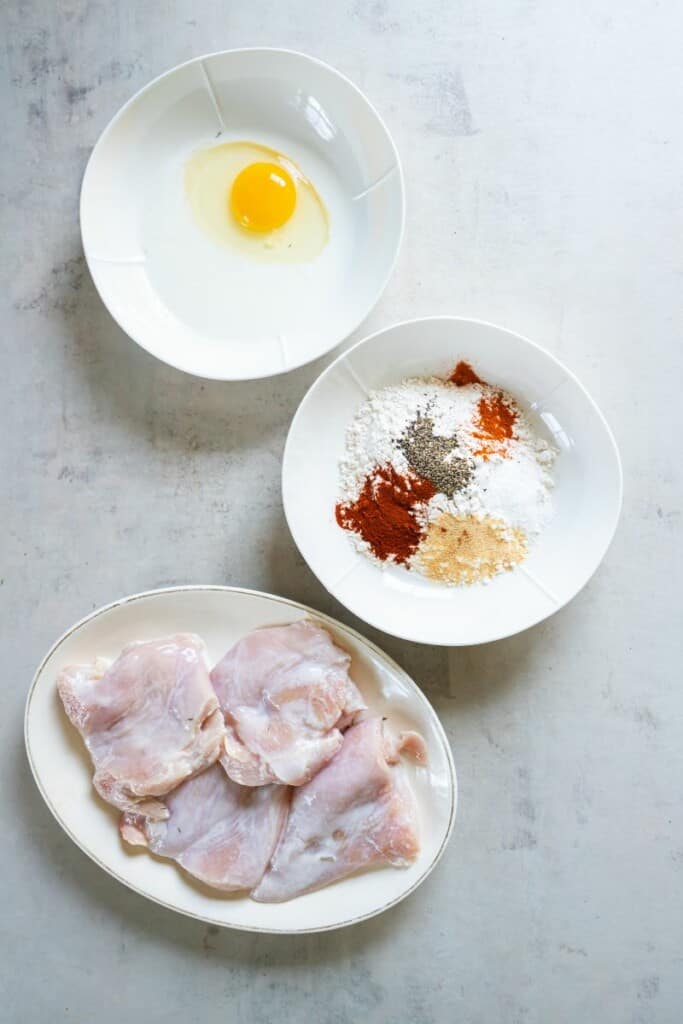 marinated chicken on a plate with a bowl of spices and egg wash