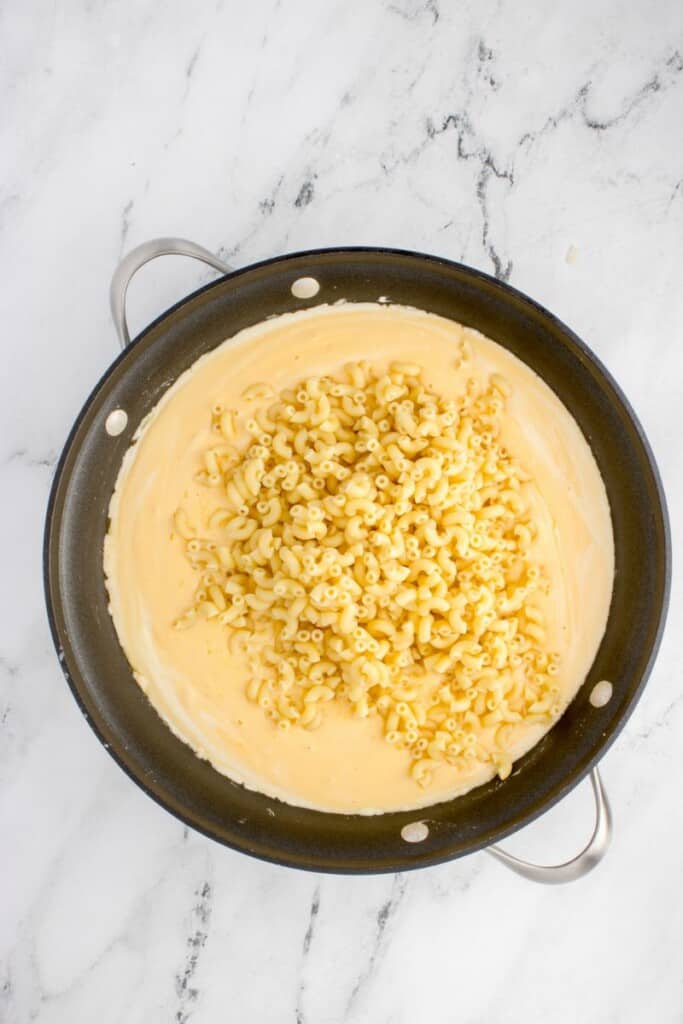 adding cooked elbow macaroni pasta to homemade cheese sauce