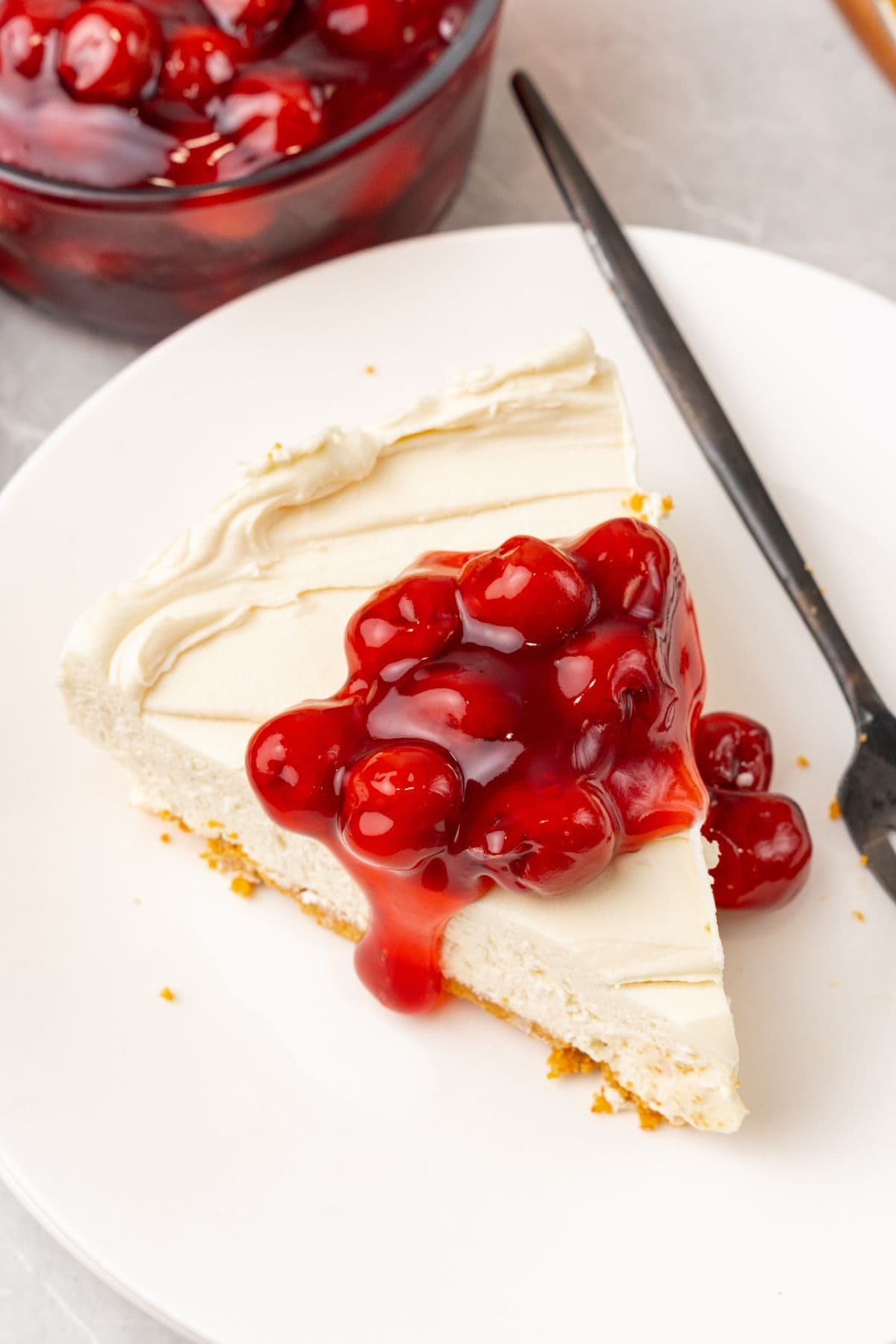 A slice of no bake cheesecake with cool whip on a plate with cherry pie filling on top.