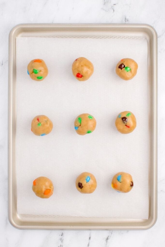 Peanut butter M and M cookies scooped out onto a cookie sheet with 9 cookies on it.