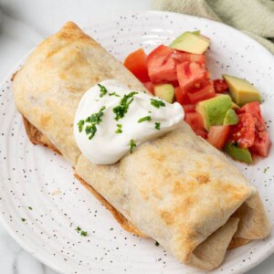 Air fried chimichanga served with sour cream and chunks of tomato and avocado.