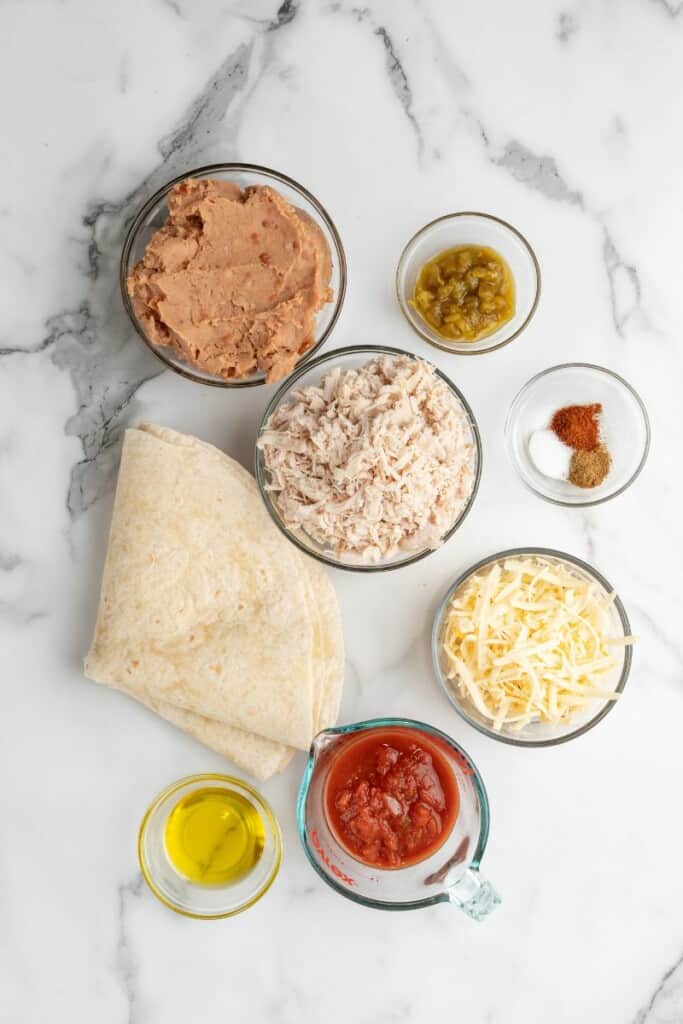 Chimichanga ingredients in clear bowls, next to a stack of tortillas.